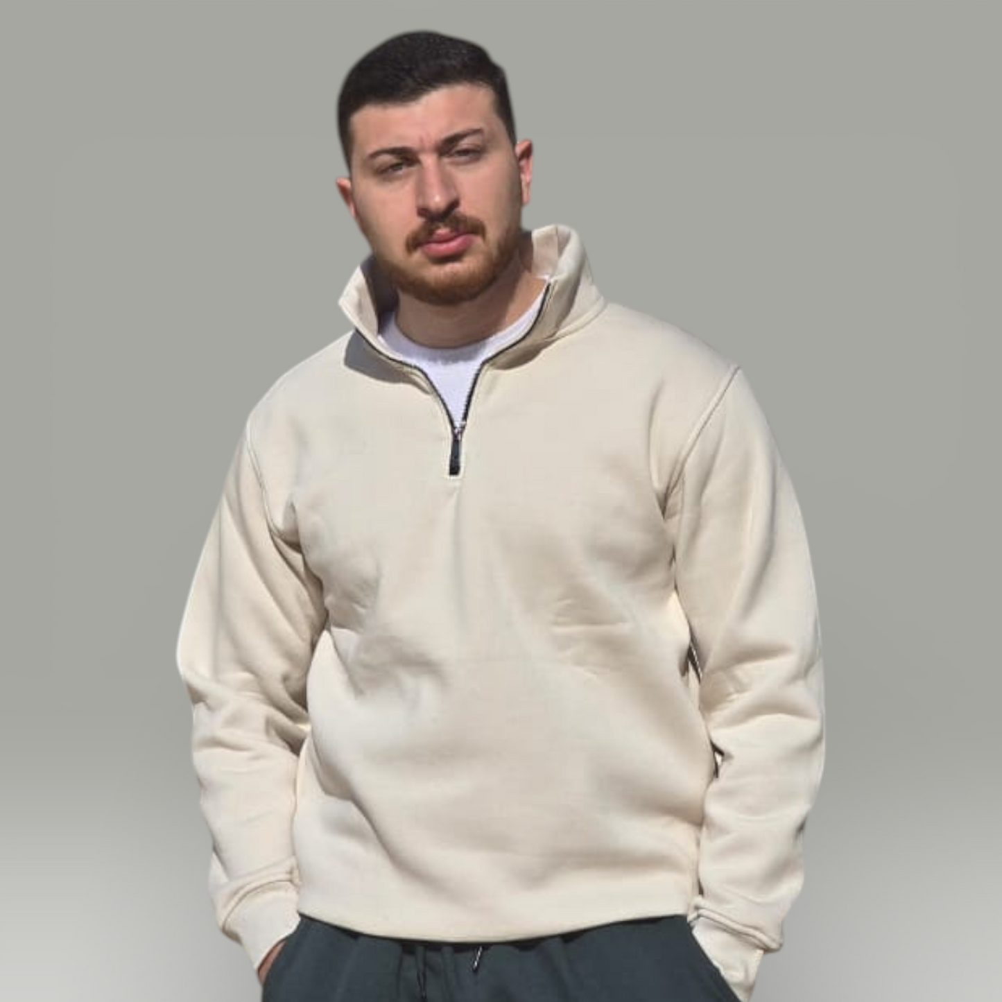 Man wearing a beige fleece pullover and dark pants against a gray background