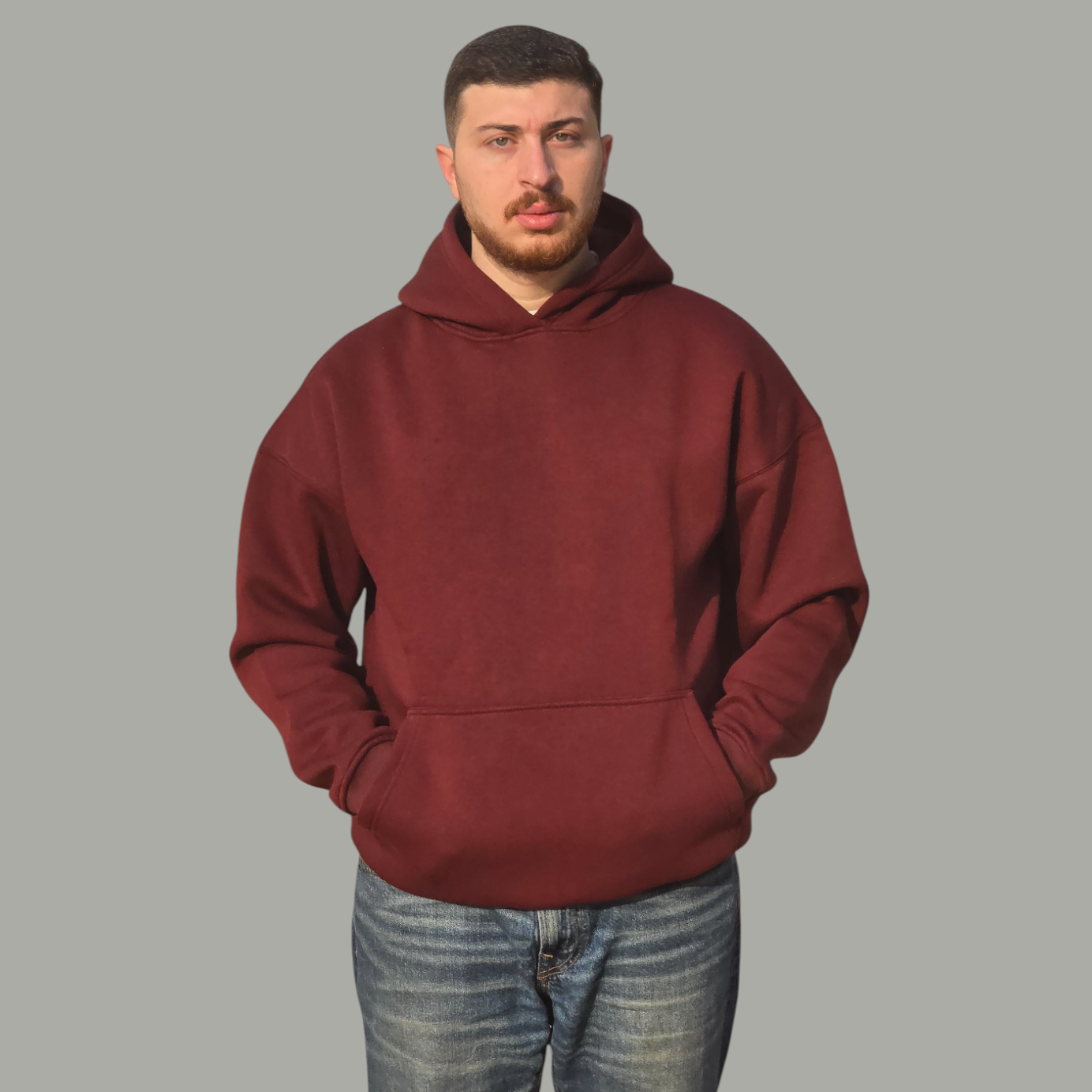 Man wearing a maroon hoodie and blue jeans on a gray background