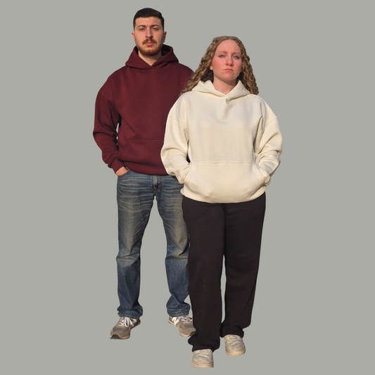 Two people wearing hoodies and jeans on a plain background