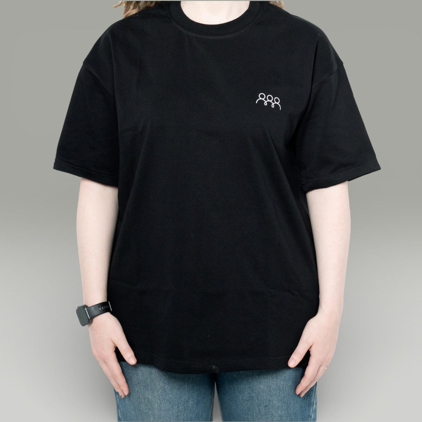Person wearing a black t-shirt with a small logo on a gray background
