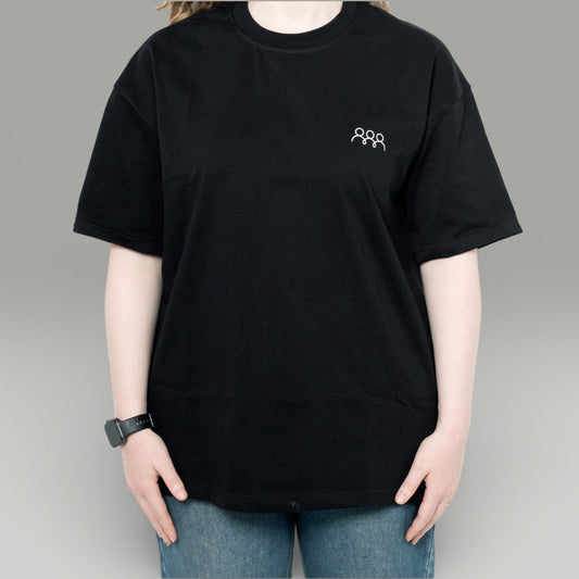 Person wearing a black t-shirt with a small logo on a gray background