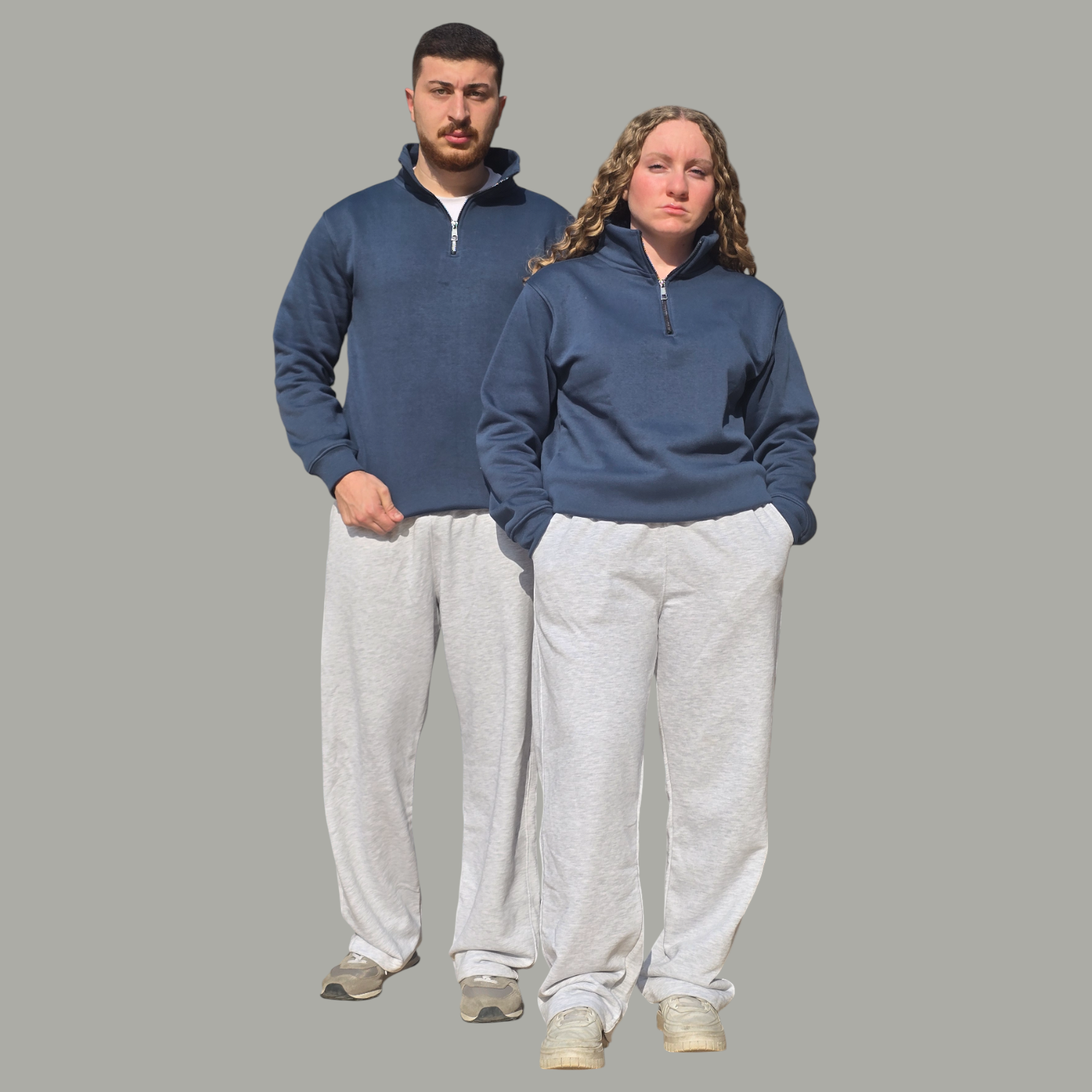 Two people wearing matching petrol pullovers and gray sweatpants on a gray background