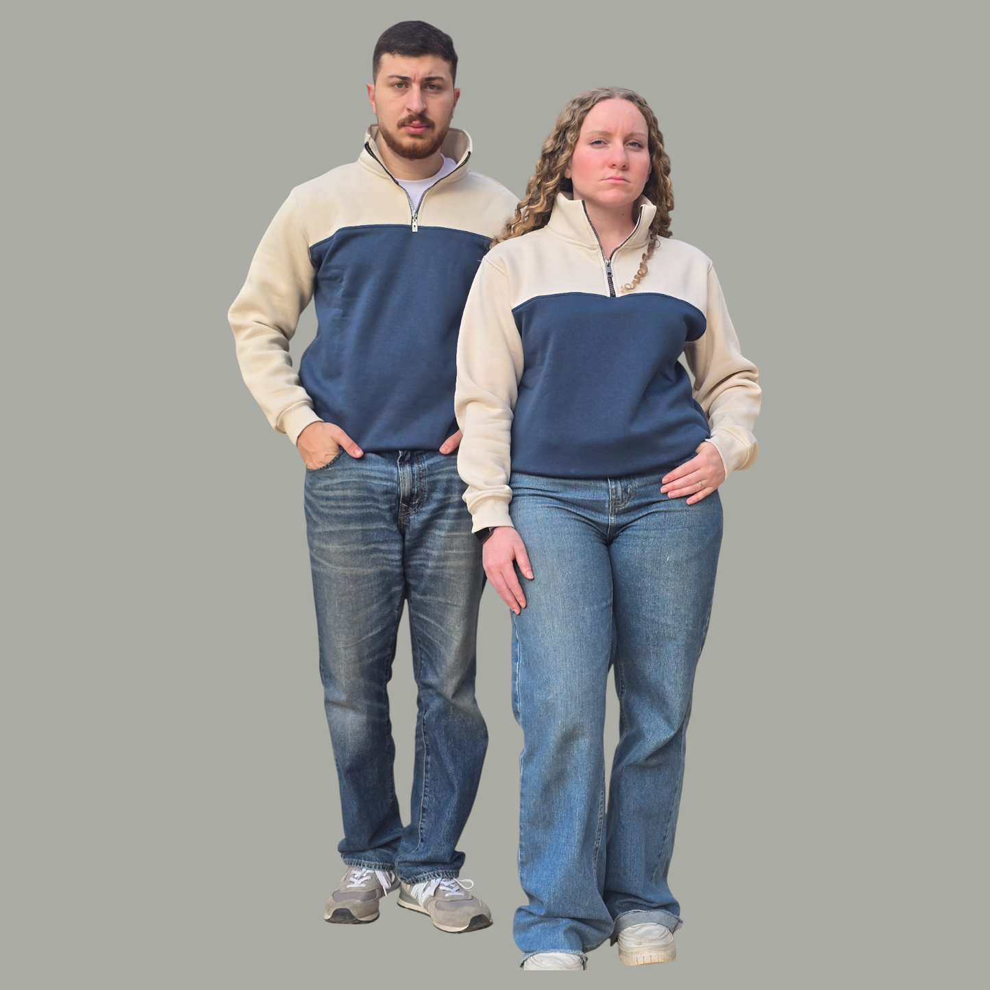 Two people wearing matching blue and beige sweaters with jeans on a gray background