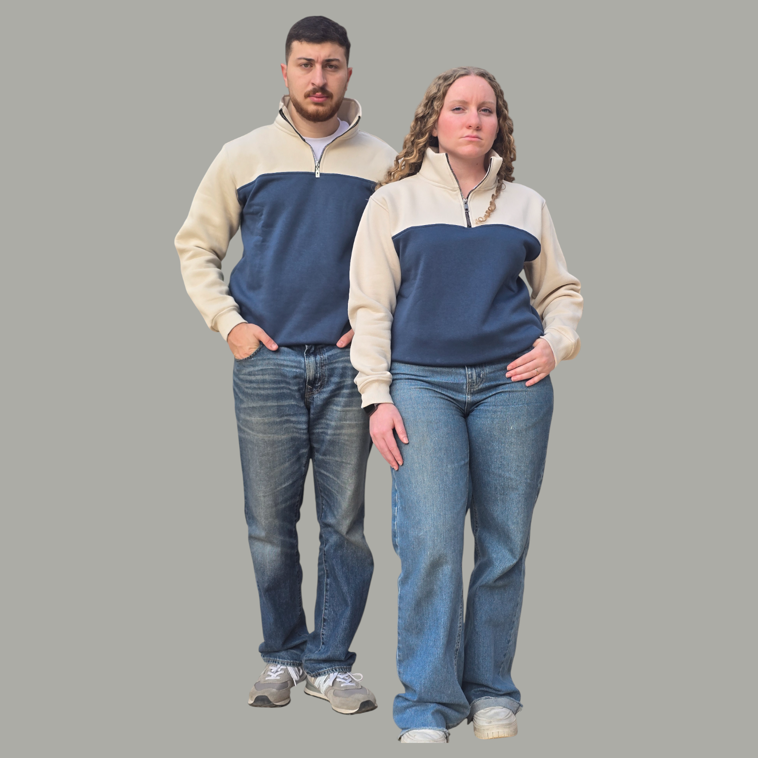 Two people wearing matching blue and beige sweaters with jeans on a gray background